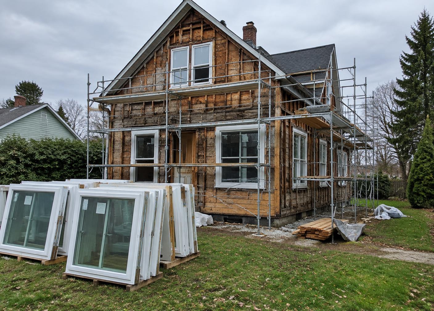 A house mid-renovation with scaffolding and new windows on the lawn